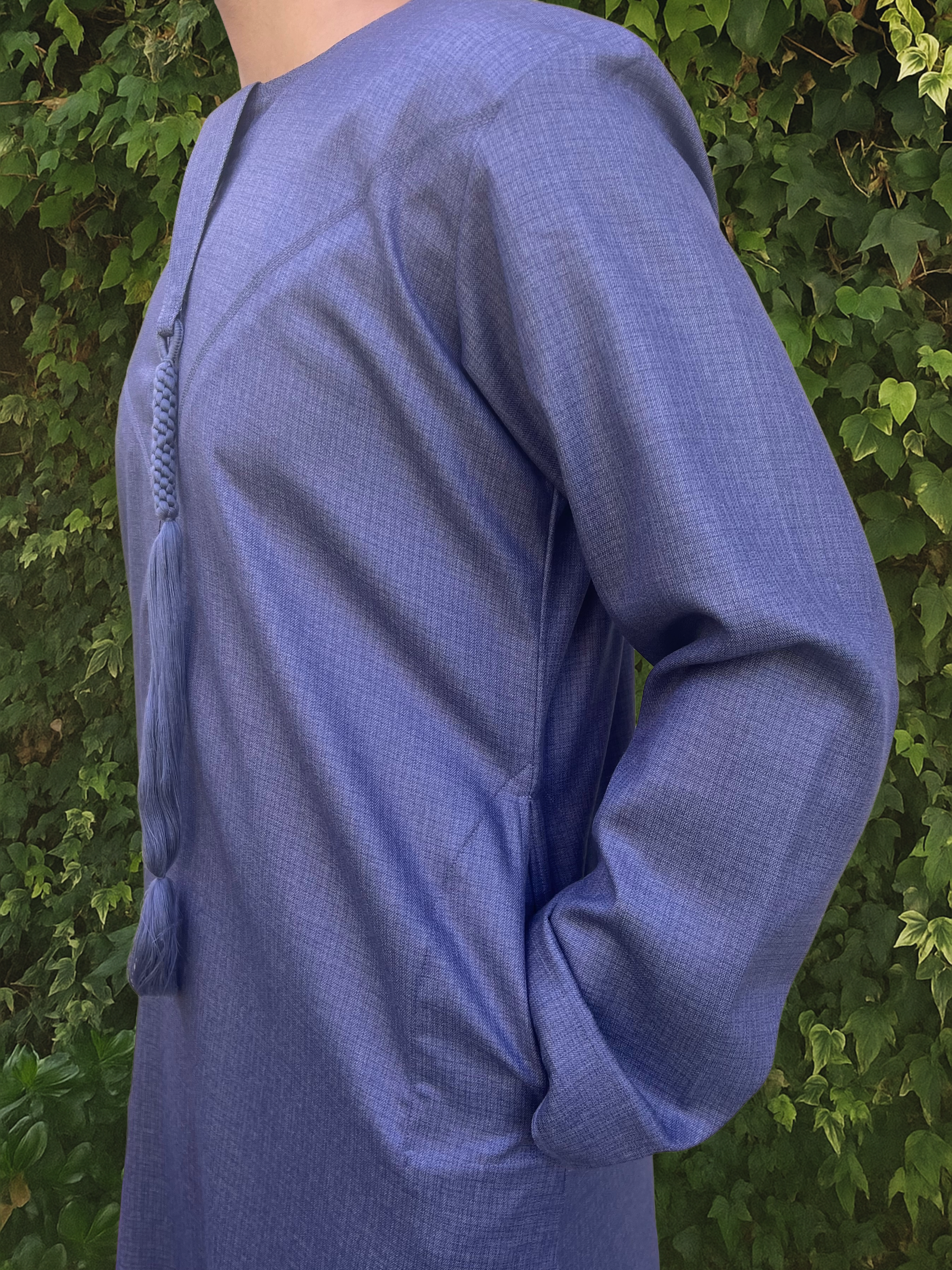 Person wearing a blue thobe against a green leafy background